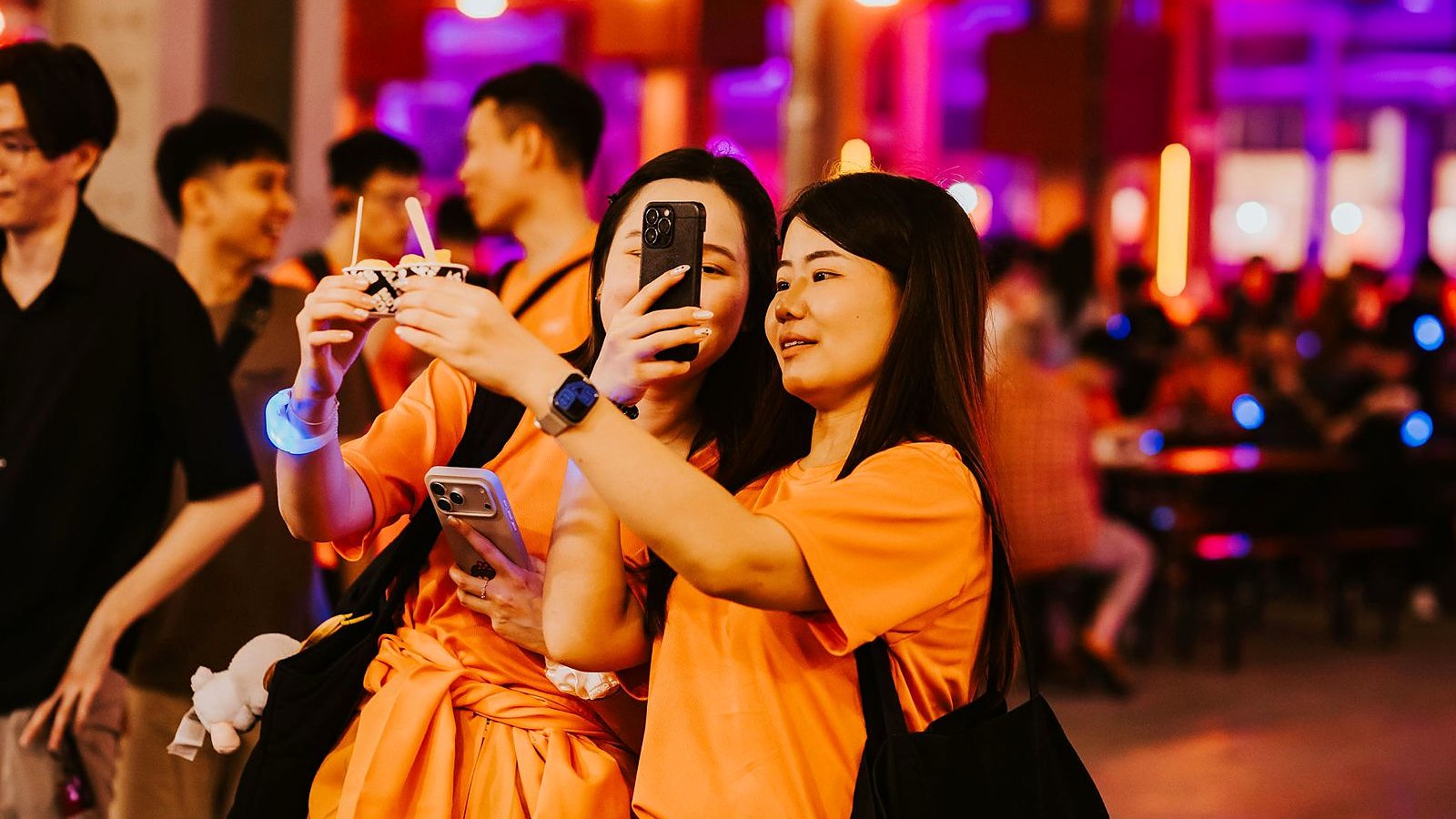 PwC event attendees in orange shirts taking selfies at a branded photobooth experience.